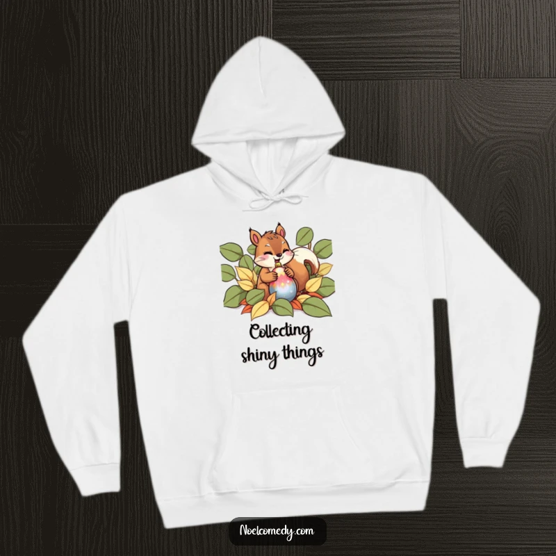 Funny Hoodie depicting a giggling squirrel tucking away a shiny Christmas ornament within a pile of leaves.