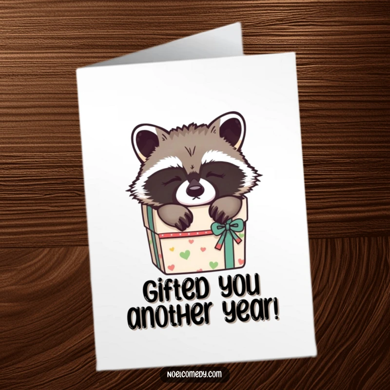 Funny Free Printable Birthday Card: A sleepy raccoon curled up adorably inside a decorated gift box, perfect for cozy birthday wishes.